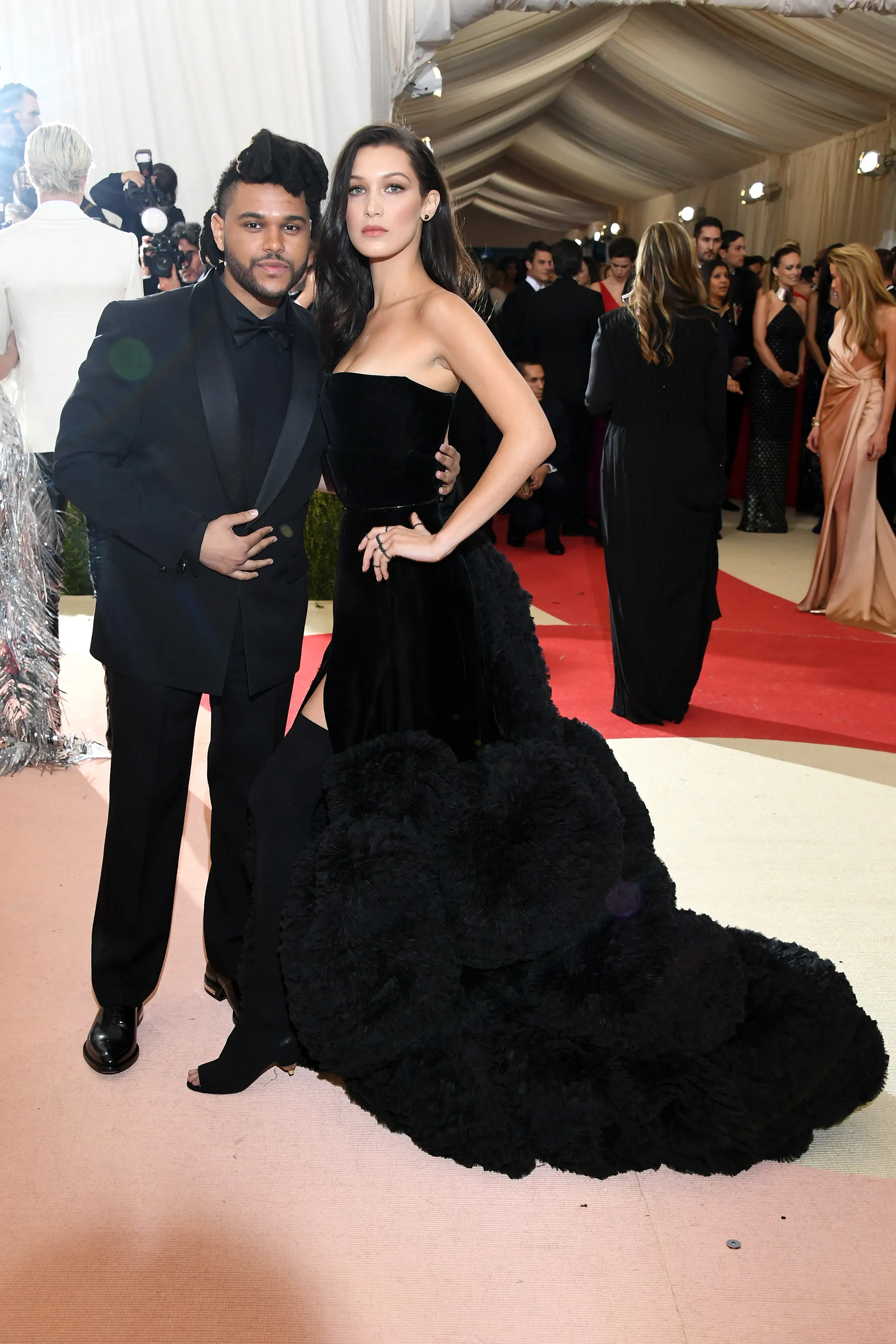 Bella Hadid in a long black dress with fur trim, and The Weeknd in a black suit.