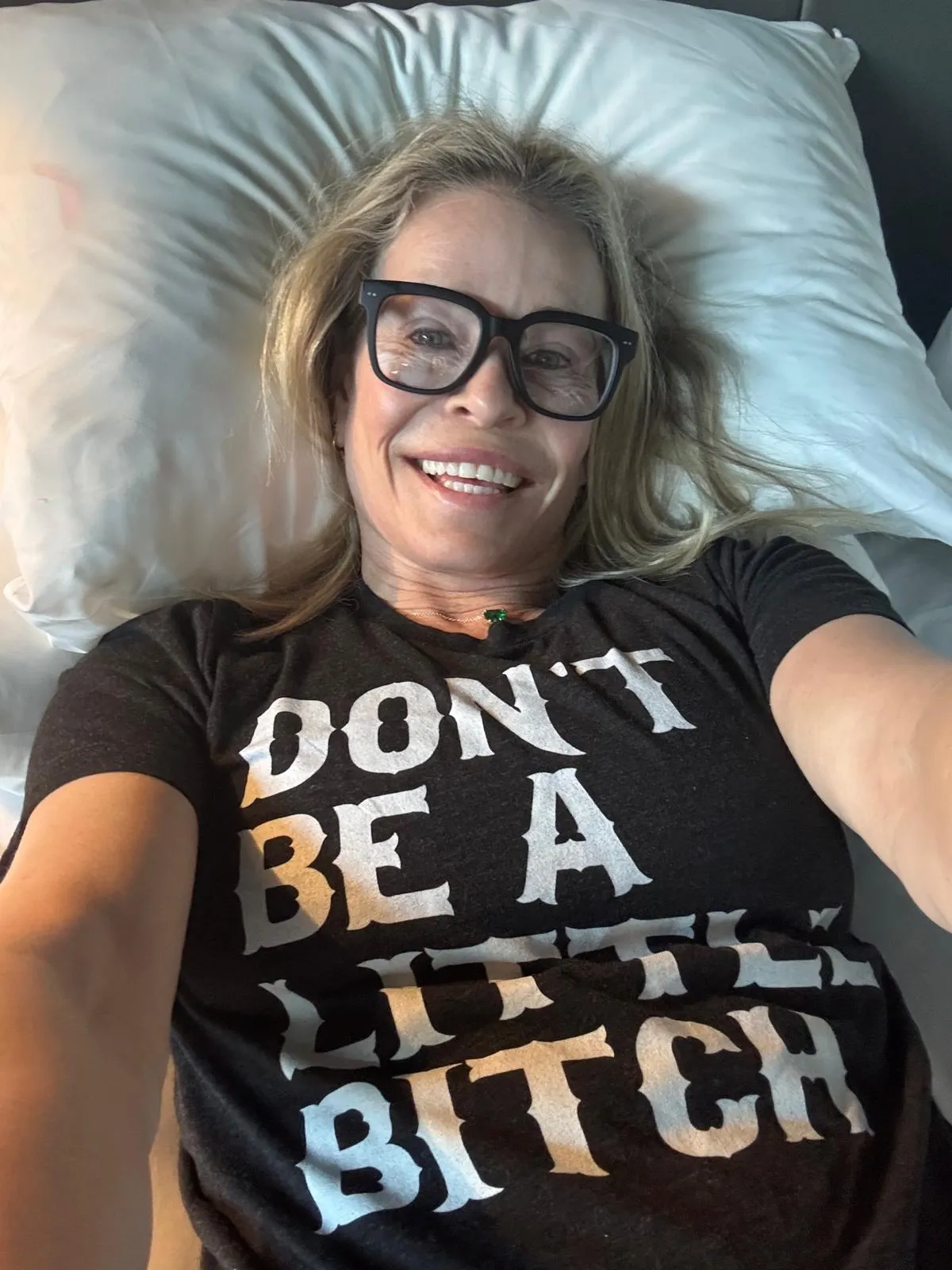 Chelsea Handler lying in bed, smiling and wearing a t-shirt that reads 