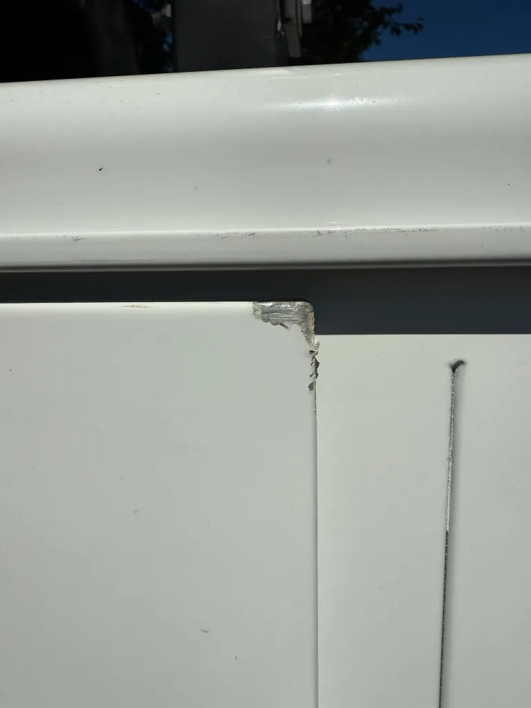 A damaged white surface, possibly a corner of a structure, with visible chipping and tearing.