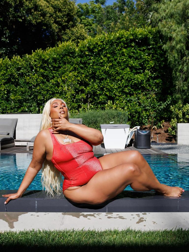 Lizzo posing in a red swimsuit by a pool.