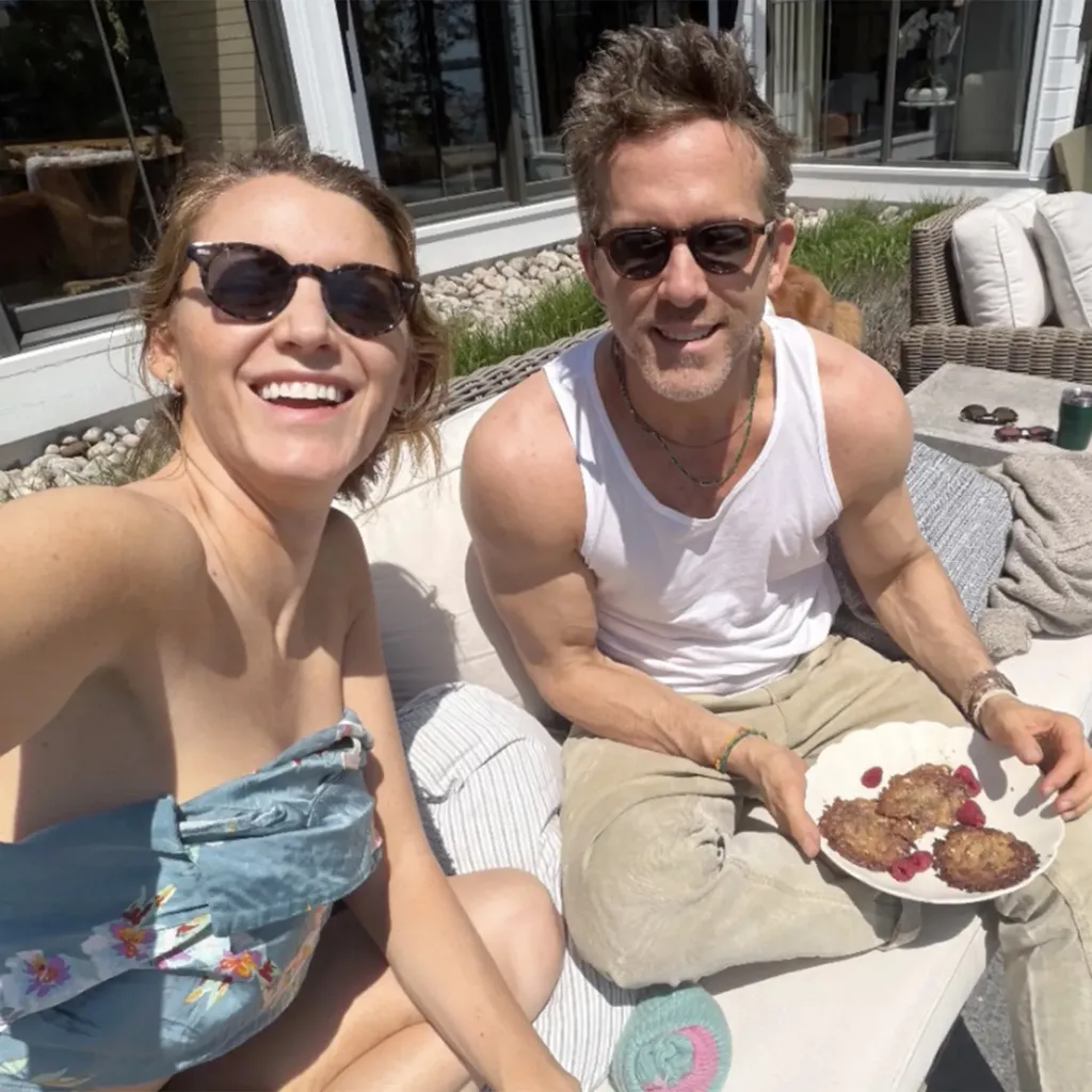 Blake Lively smiling and Ryan Reynolds in a white tank top holding a plate of food.