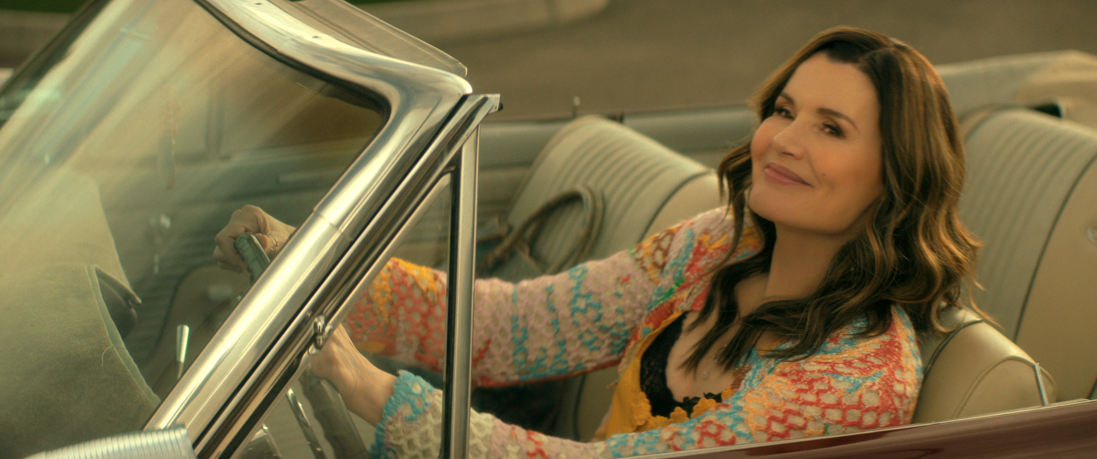 Geena Davis as Renee in The Boroughs, smiling while driving a car.