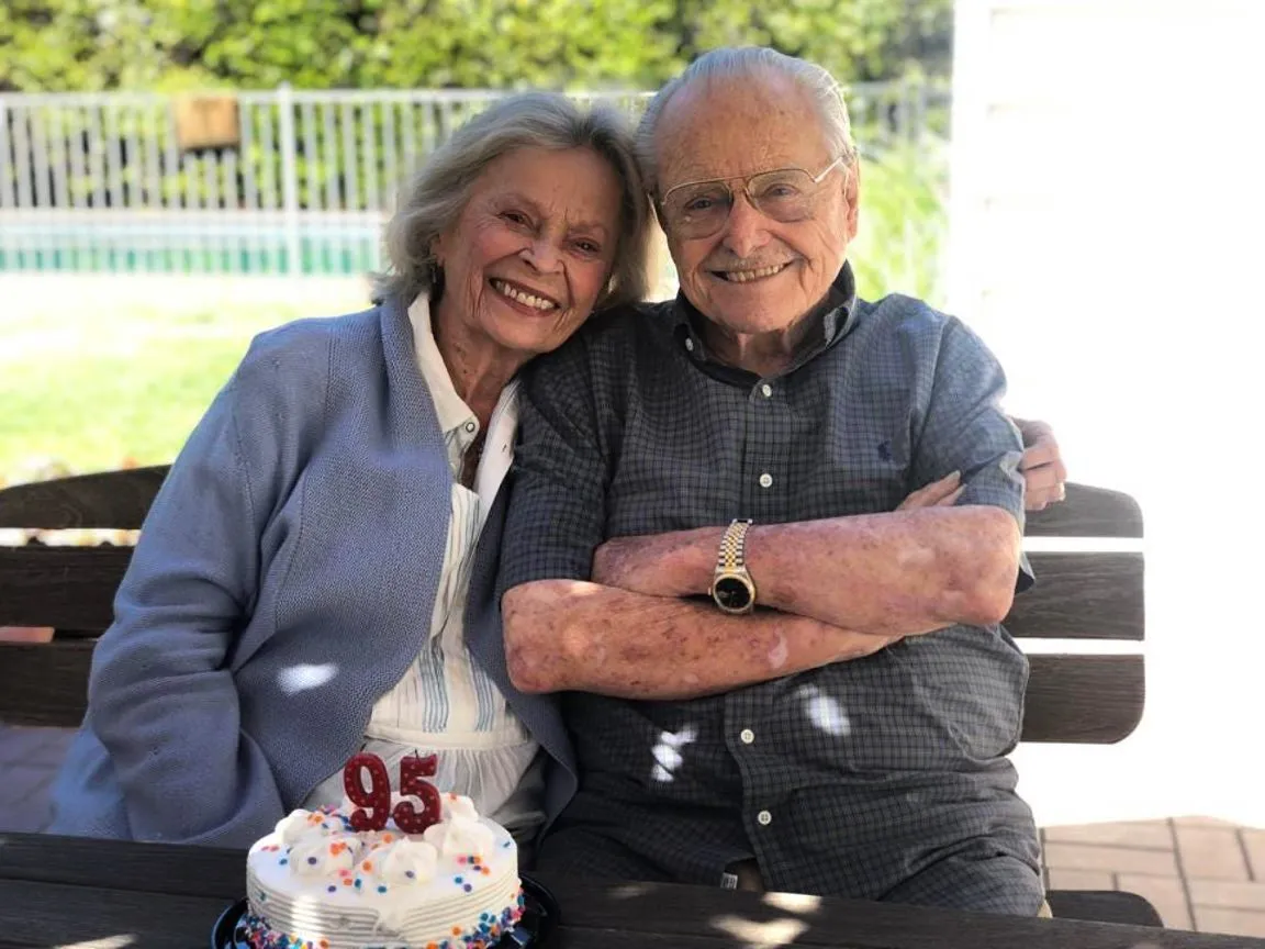 William Daniels and Bonnie Bartlett smiling with a birthday cake with the number 95 candle.