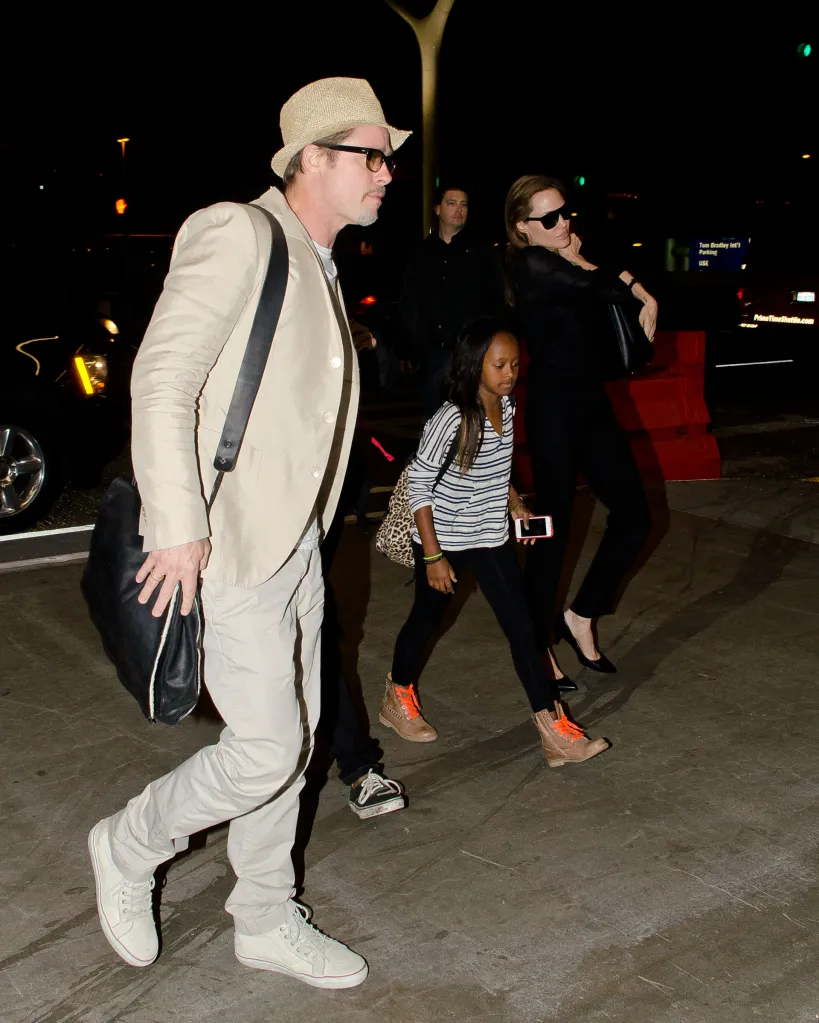 Brad Pitt, Maddox Jolie-Pitt, Zahara Jolie-Pitt, and Angelina Jolie walk through an airport at night.