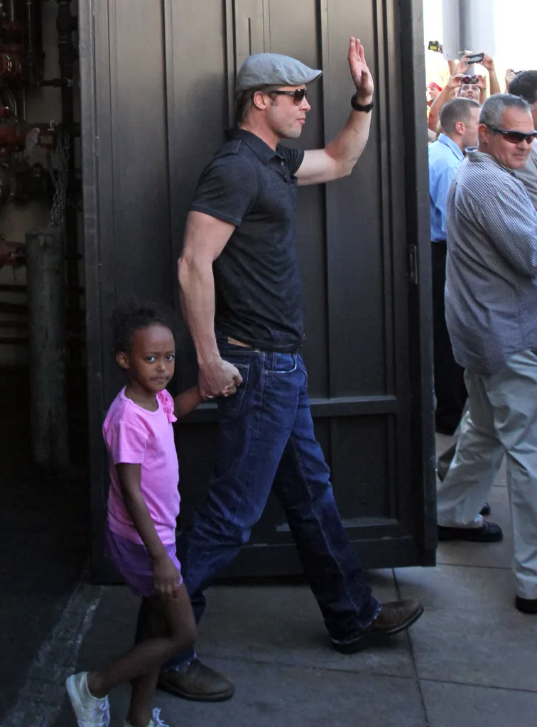 Brad Pitt waves while holding Zahara Jolie-Pitt's hand.