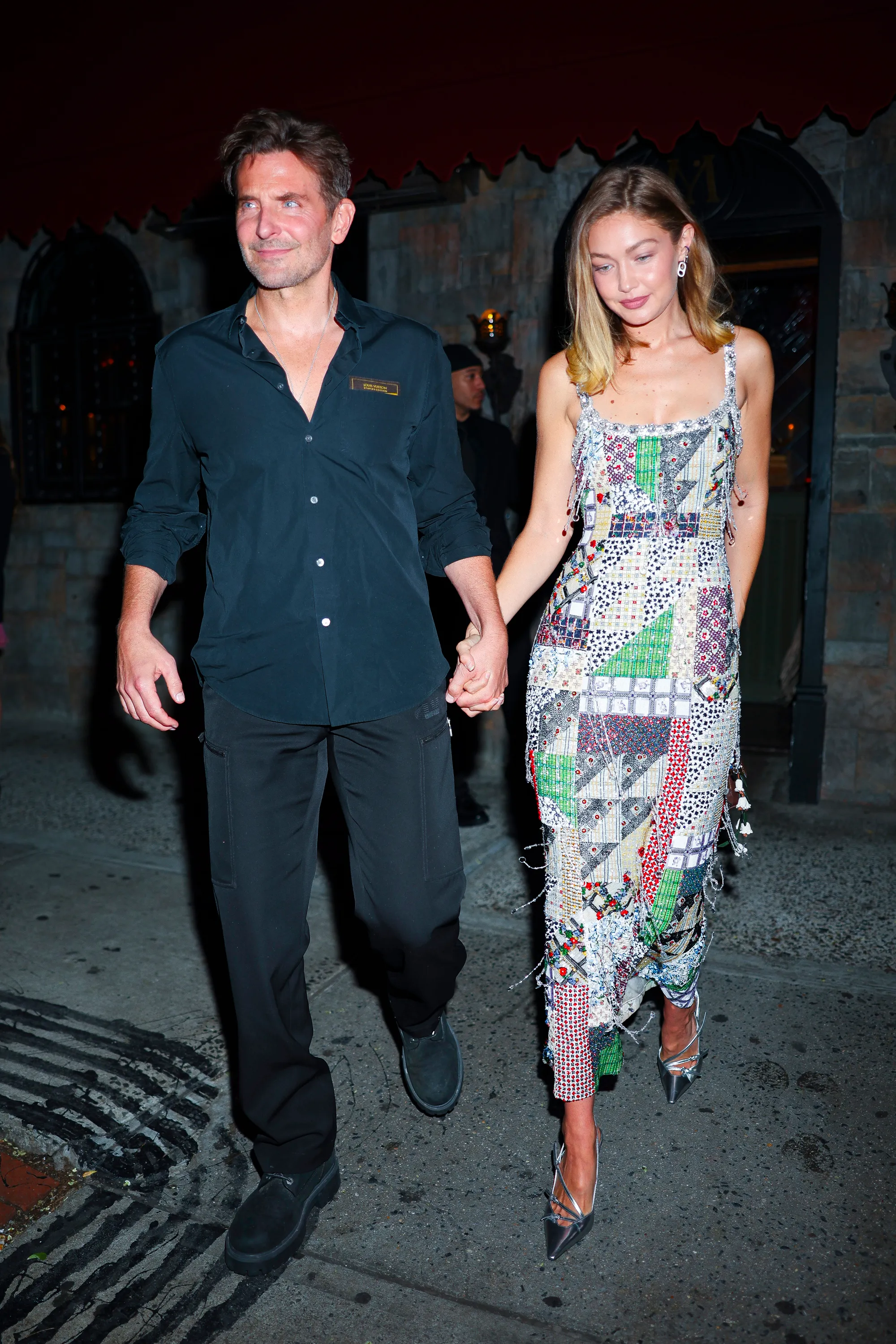 Bradley Cooper and Gigi Hadid holding hands, walking down the street at night.
