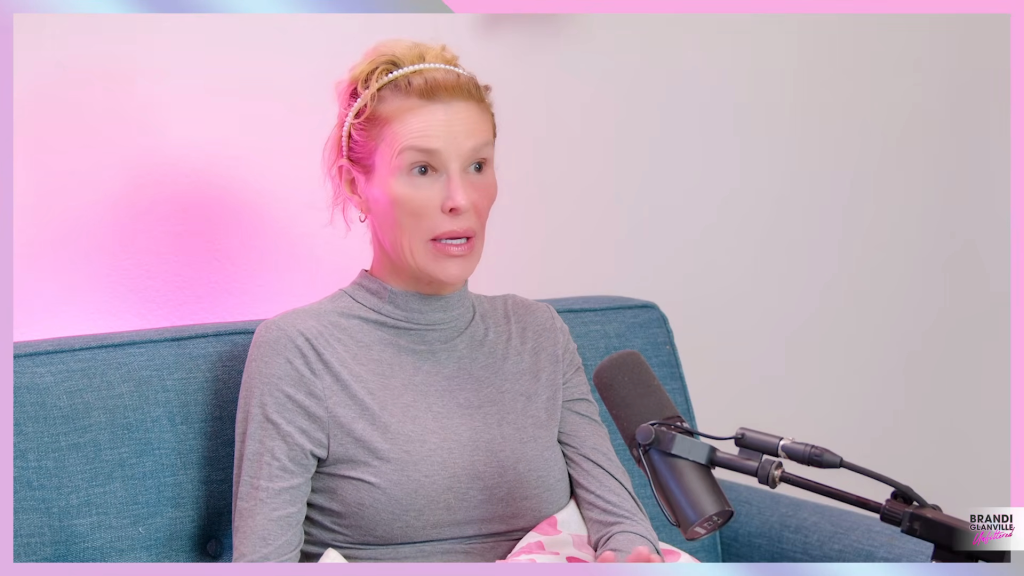 Brandi Glanville sitting on a blue couch, speaking into a microphone.