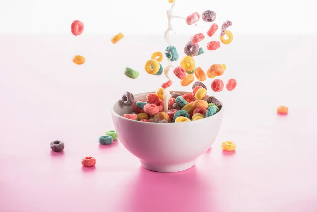 Bright multicolored breakfast cereal in a bowl with milk splash on a pink background.