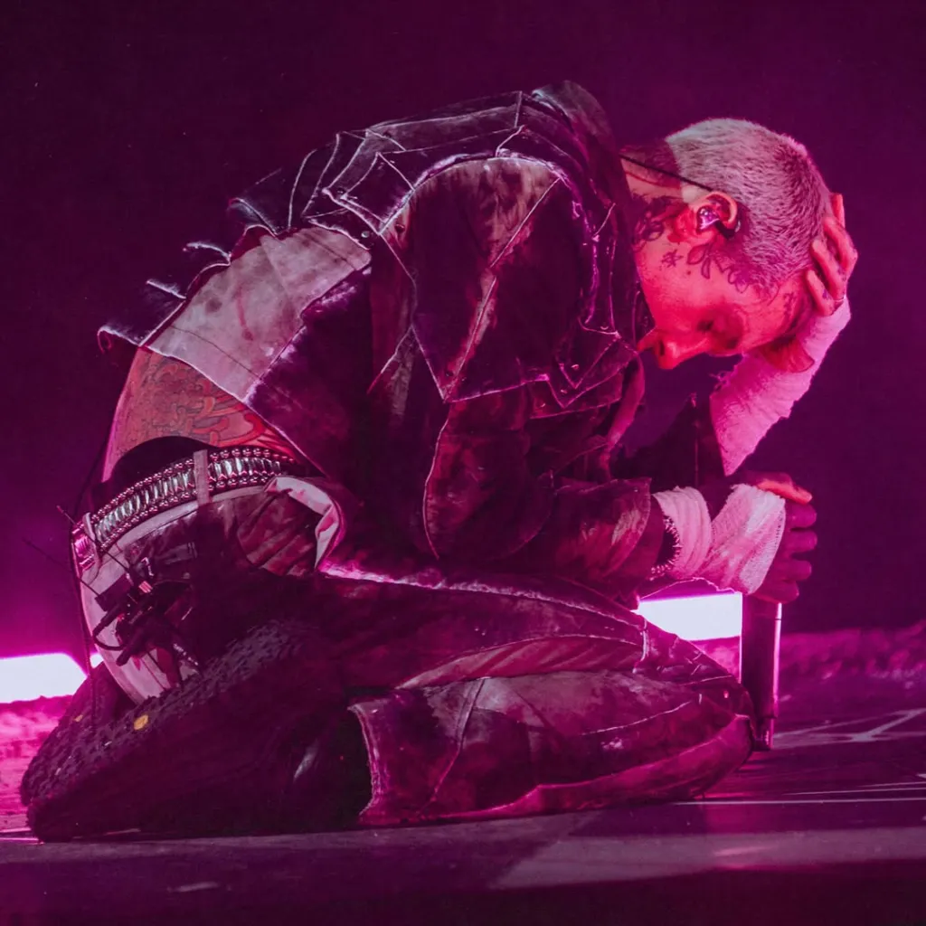 Bring Me The Horizon frontman Oli Sykes kneeling on stage with his head in his hand after being hit by a phone.