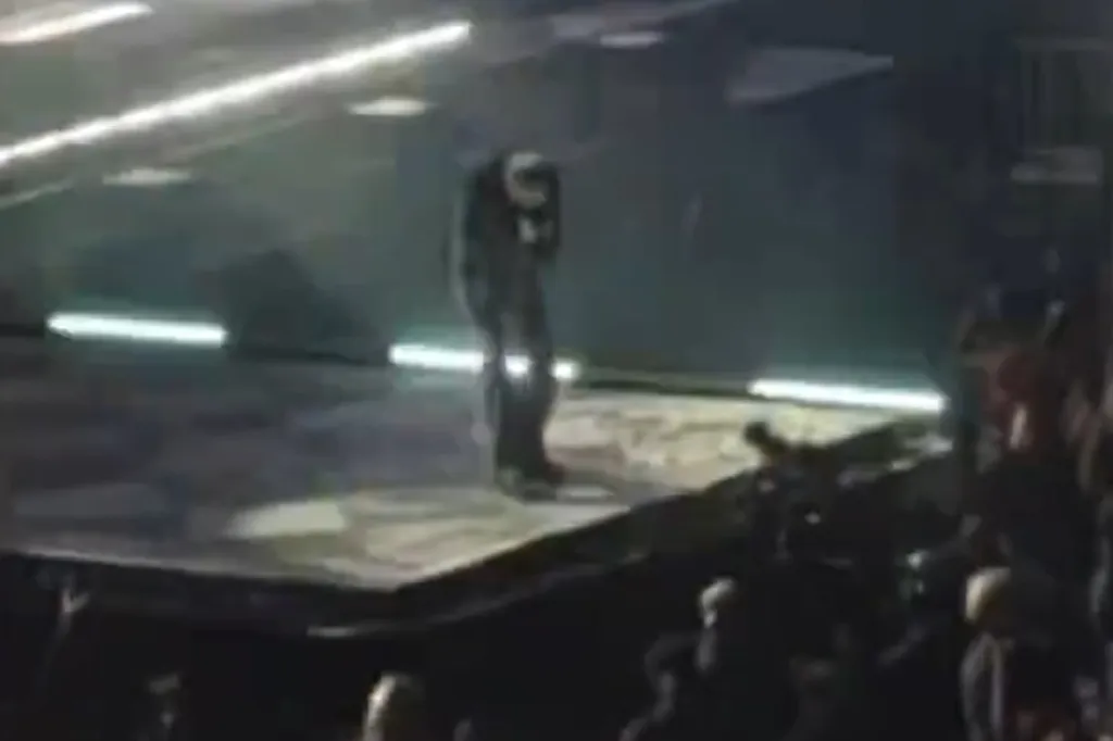 Oli Sykes on stage holding his head after being struck by a phone.