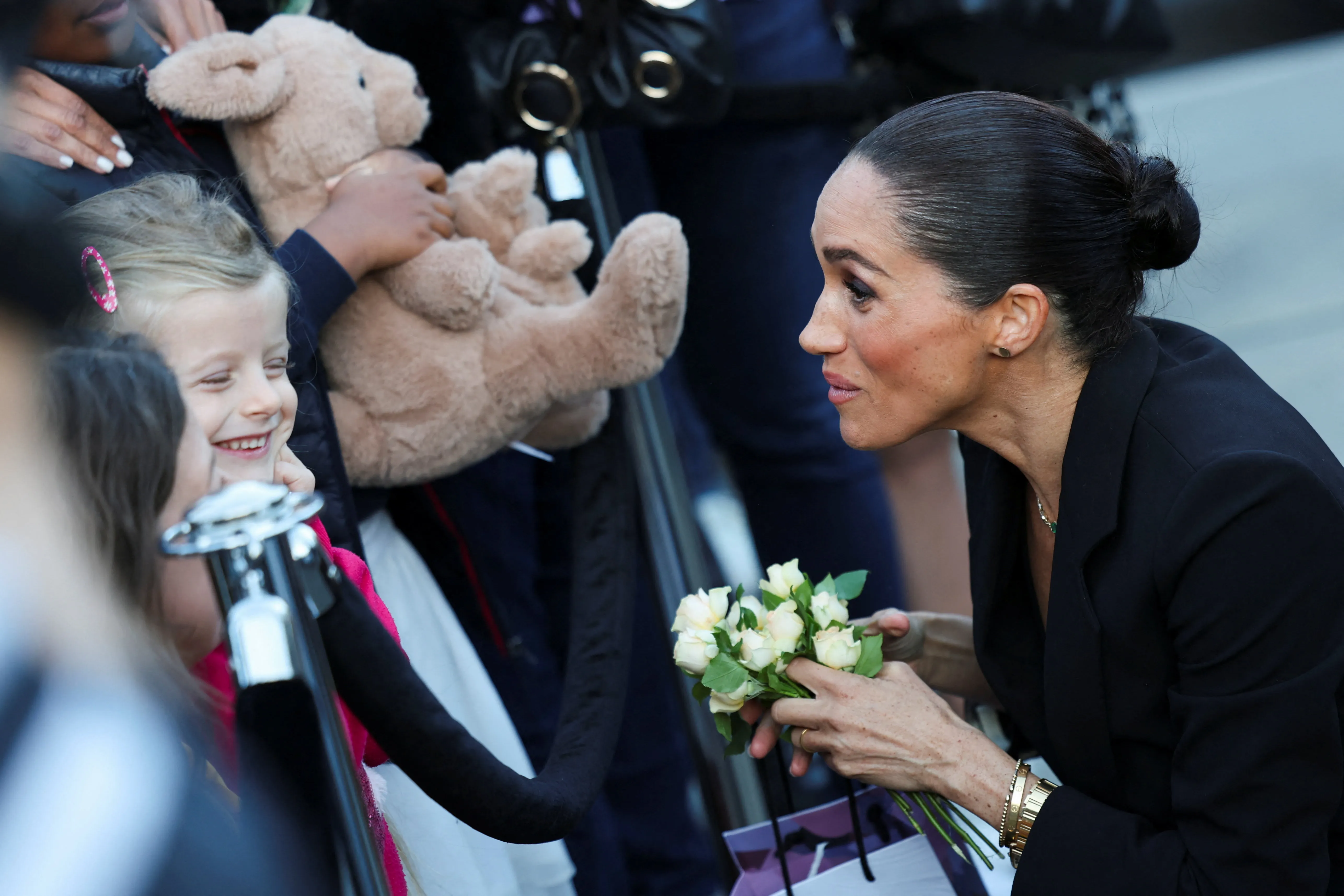 Meghan Markle talks to a child who is smiling and holding a teddy bear.