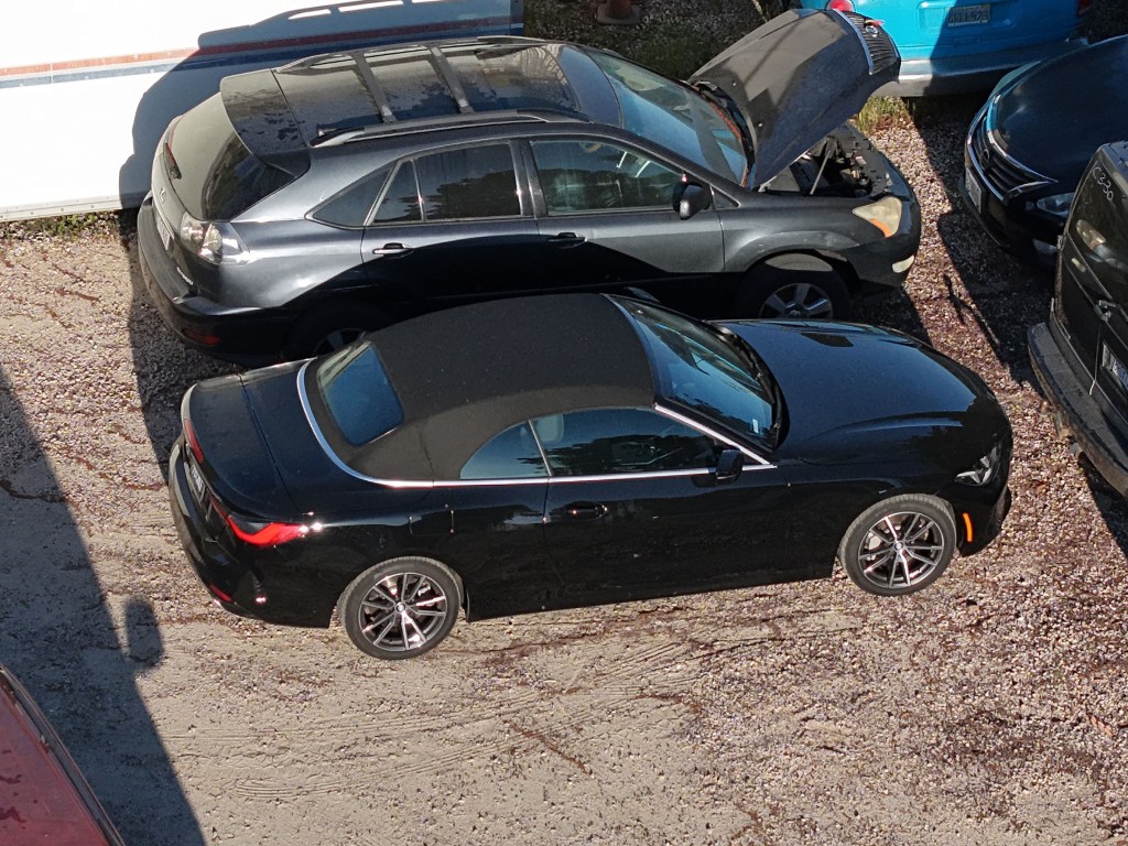 Britney Spears' black convertible and a gray SUV with its hood up, parked in a tow yard.