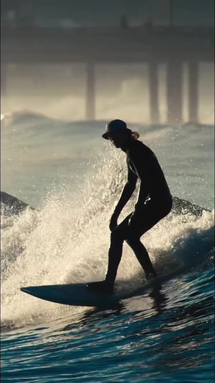 A surfer in a wetsuit and hat riding a wave.