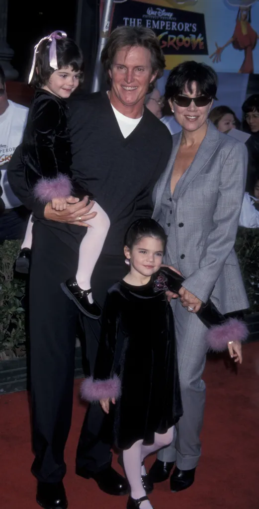 Caitlyn Jenner holding a young Kendall Jenner, with Kris and Kylie Jenner beside them, on a red carpet.