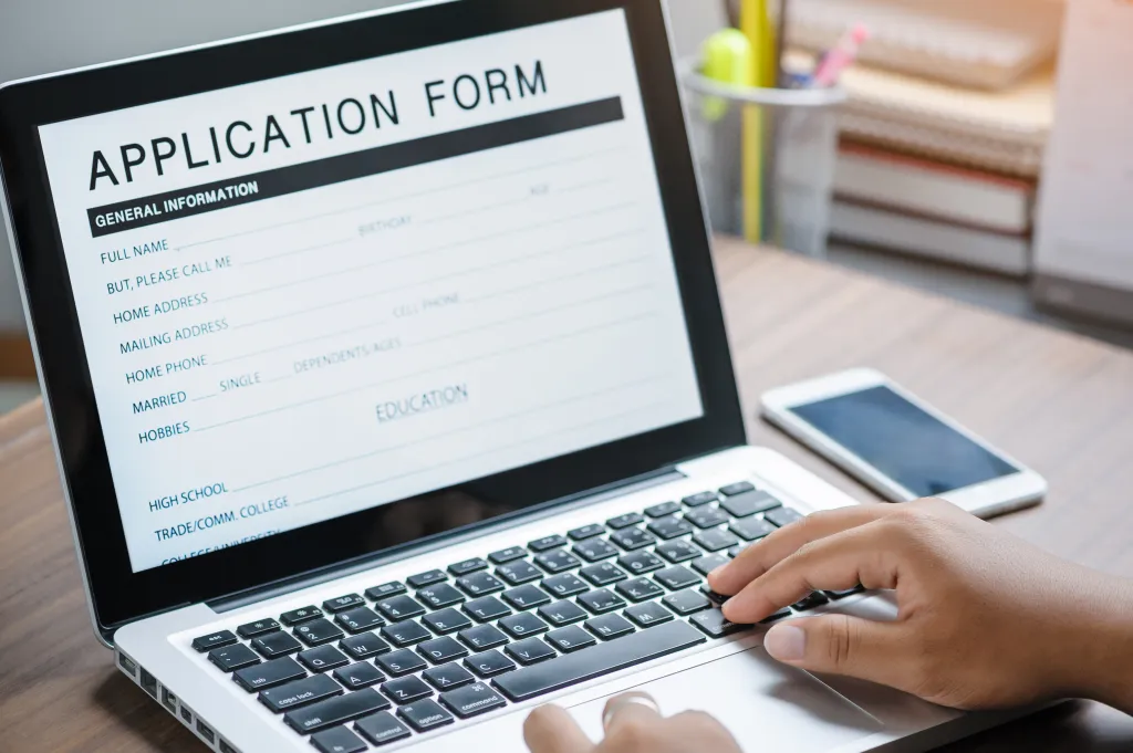 Hands typing on a laptop with an application form on the screen.