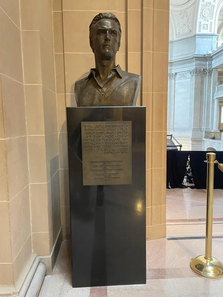 Bronze bust of Gavin Newsom on a dark pedestal with an inscribed plaque in a large hall.