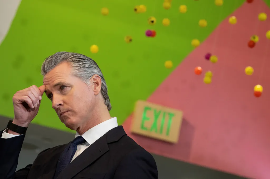 California Governor Gavin Newsom looks on, hand to his forehead, during a press conference.