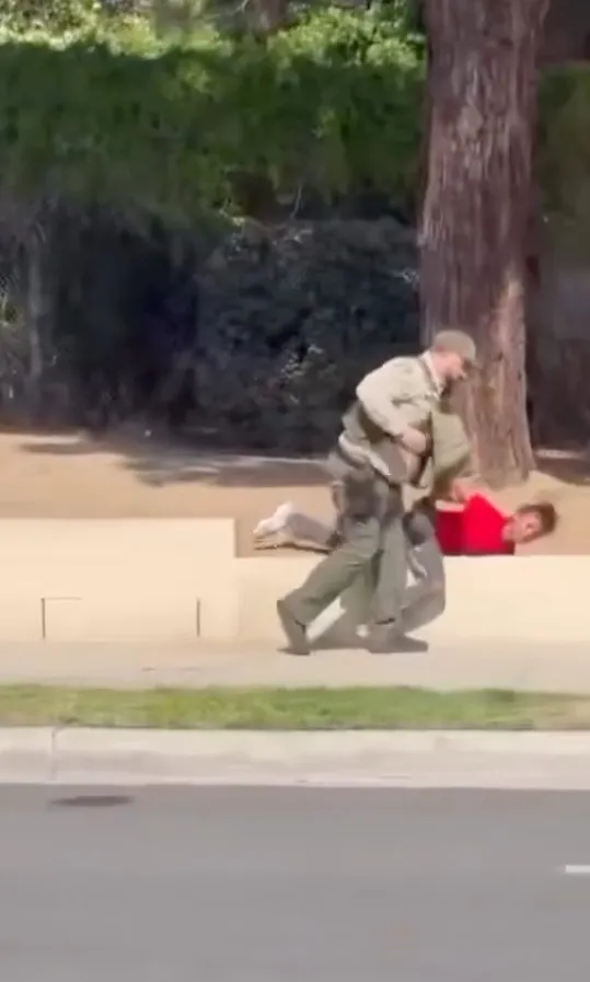 A school resource deputy holding a juvenile in a red shirt on the ground.