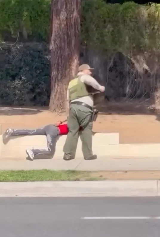 A deputy stands over a juvenile lying on the ground.