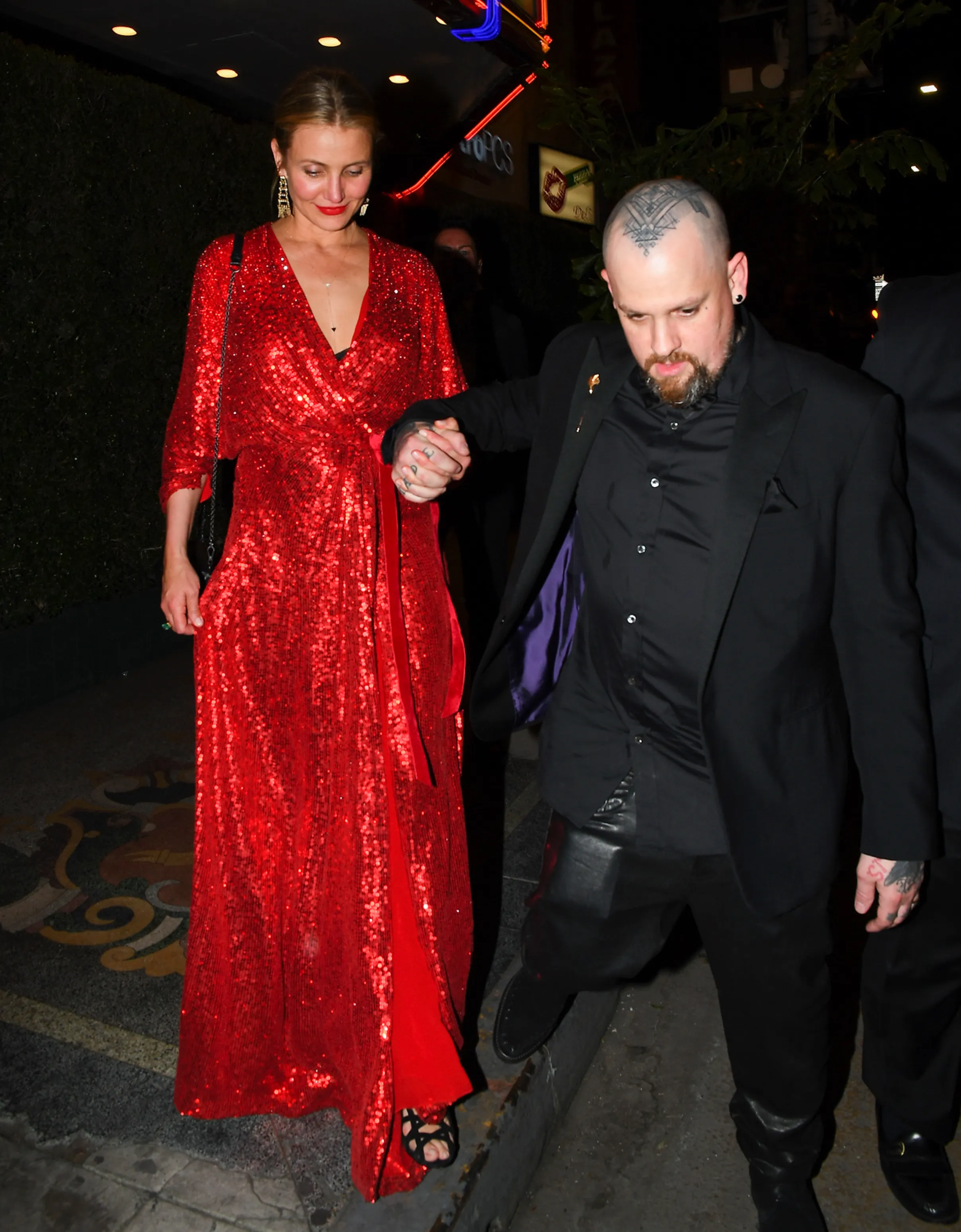 Cameron Diaz in a red sequined dress and Benji Madden in a black suit holding hands.
