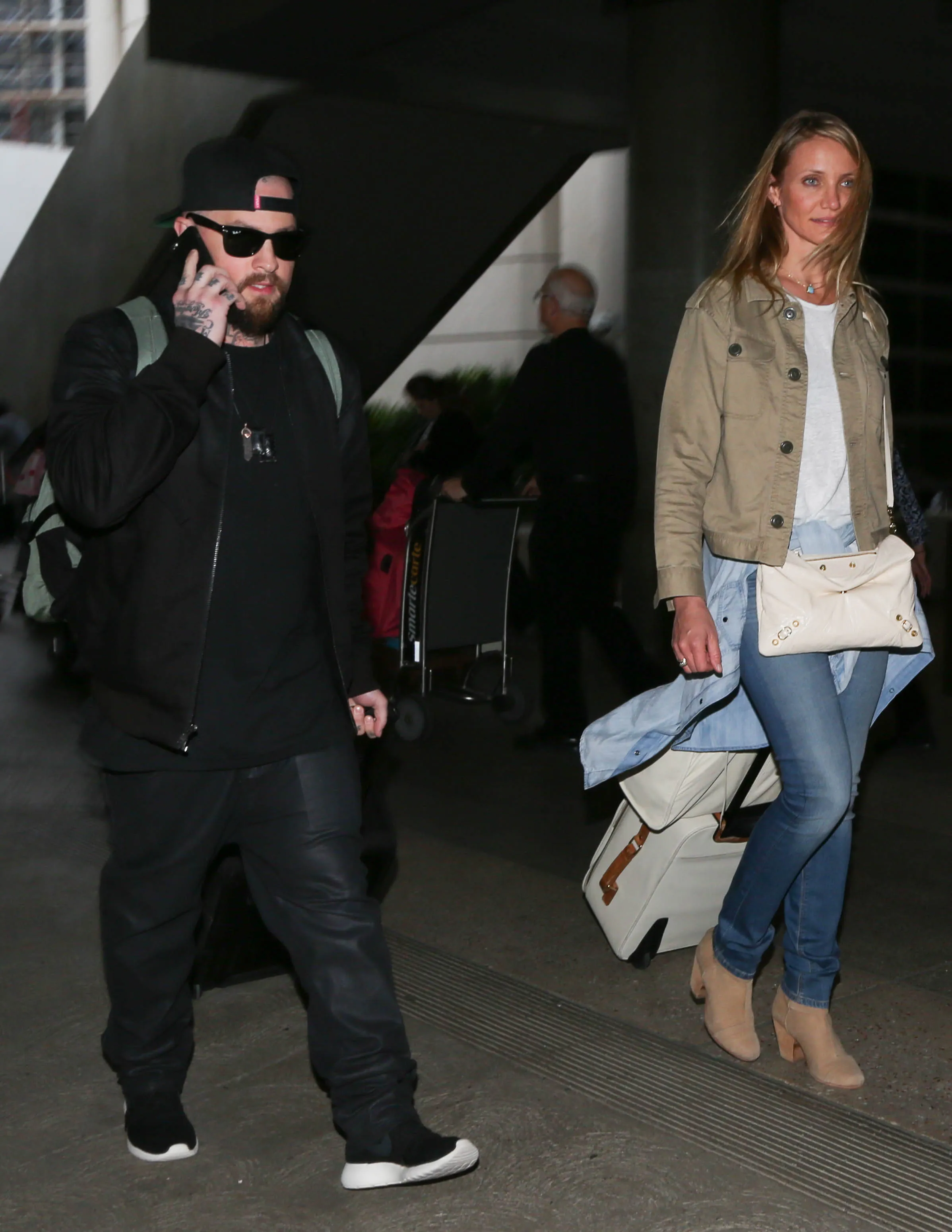 Benji Madden and Cameron Diaz walking through an airport with luggage.