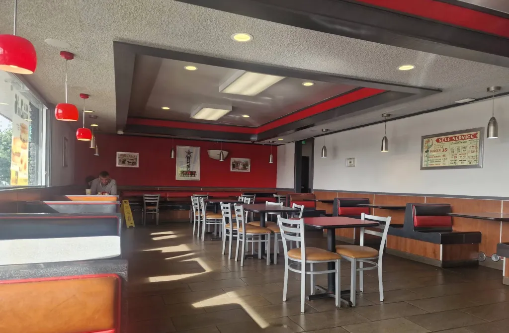 Interior of a Carl's Jr. restaurant with red accents, featuring booths, tables, and a menu board with 