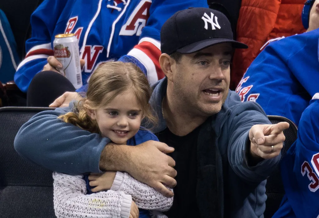 Carson Daly holding Etta Daly and pointing while watching a Pittsburgh Penguins vs. New York Rangers game.