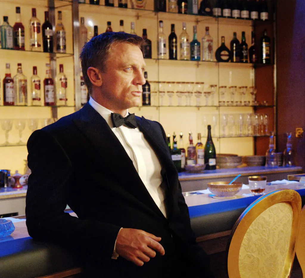 Daniel Craig as James Bond in Casino Royale (2006), leaning against a bar, looking away from the camera.