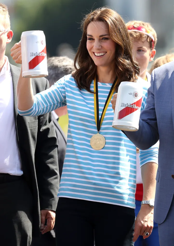 Catherine, Duchess of Cambridge, smiling and holding two Heidelberg beer steins, with a gold medal around her neck.