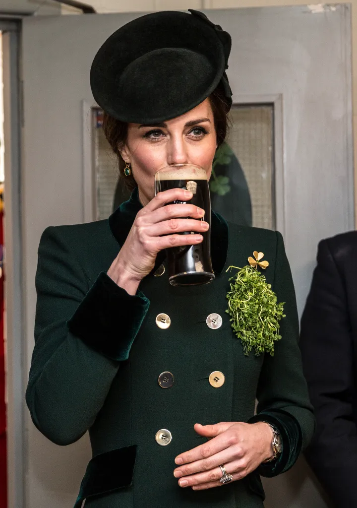 Catherine, Duchess of Cambridge, takes a drink of Guinness, wearing a green coat and hat with a shamrock brooch.