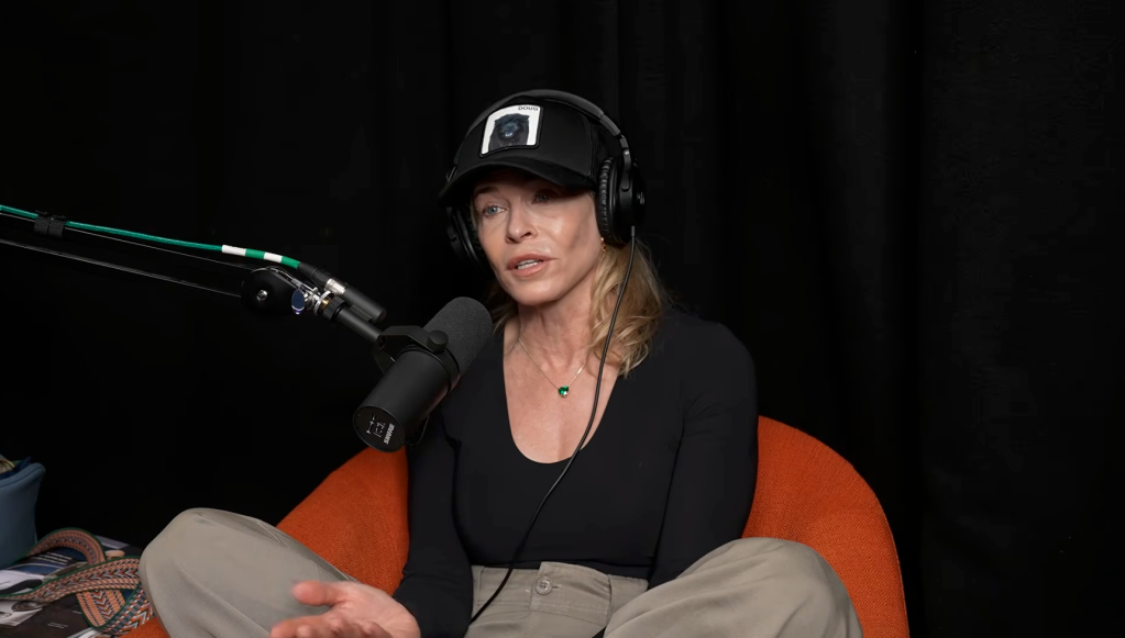 Chelsea Handler speaking into a microphone while wearing a black hat and headphones.