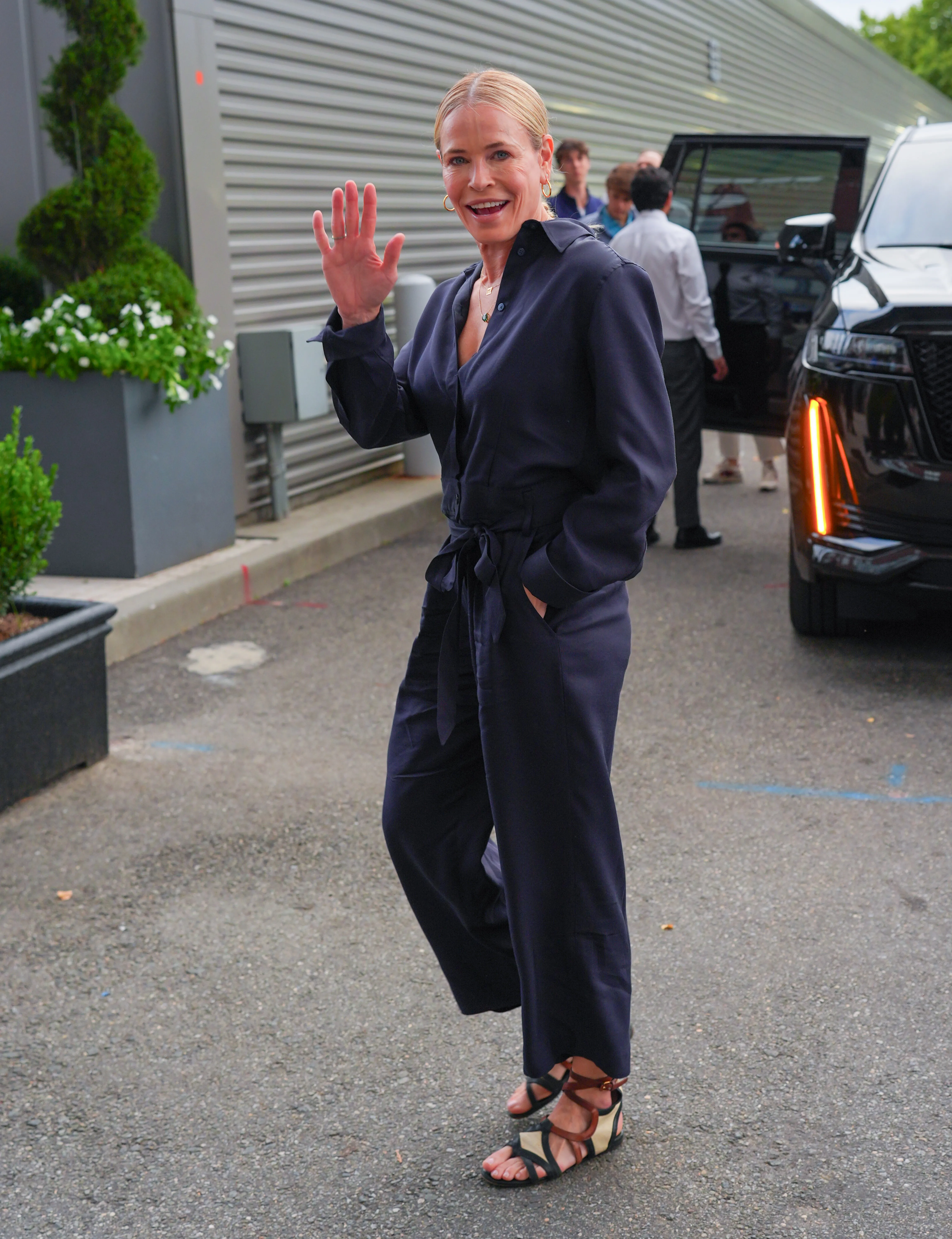 Chelsea Handler in a navy jumpsuit waves to the camera.