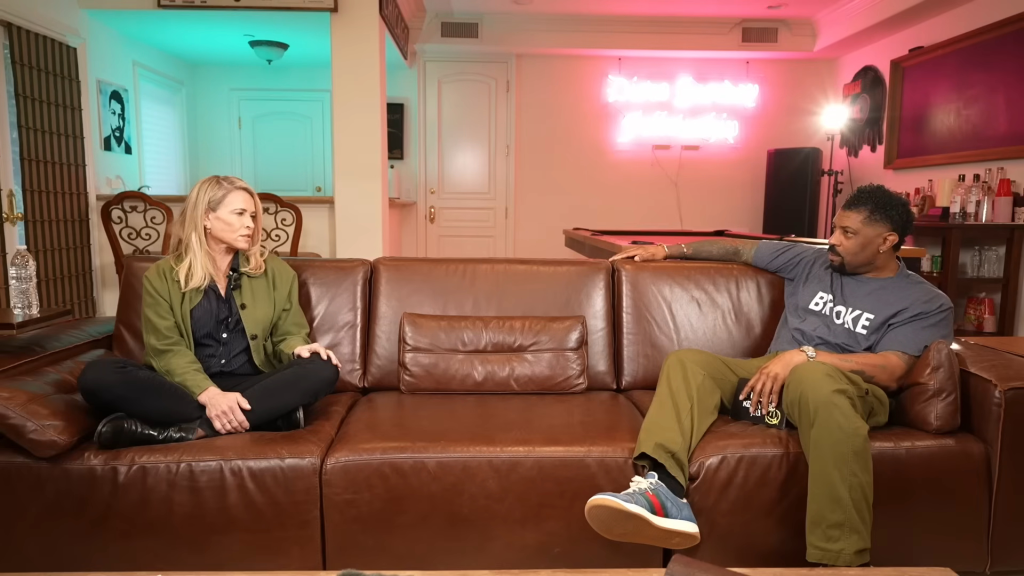 Chelsea Handler and Deon Cole sitting on a brown leather couch.