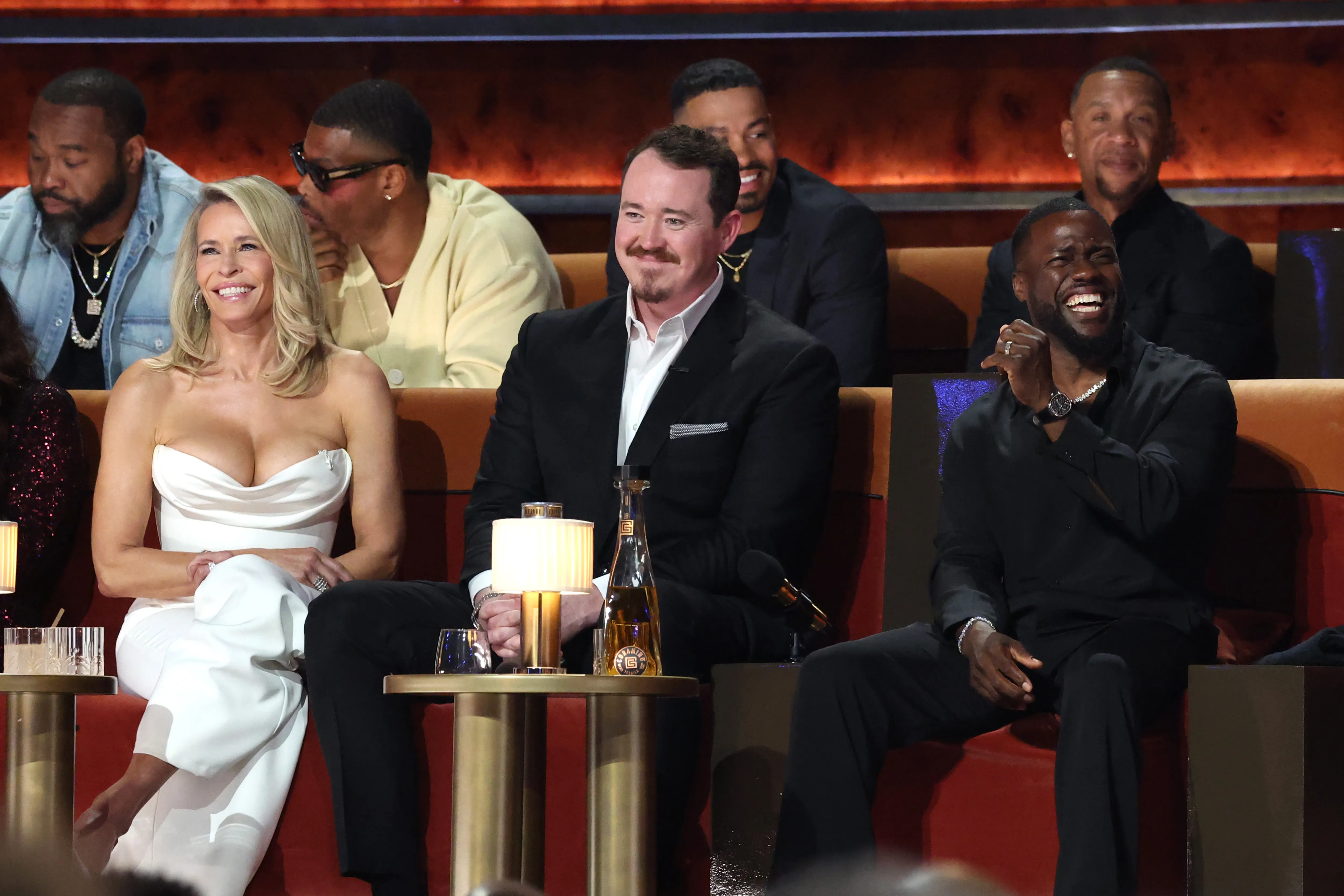 Chelsea Handler, Ron Boss Everline, and Kevin Hart sit on red couches during 