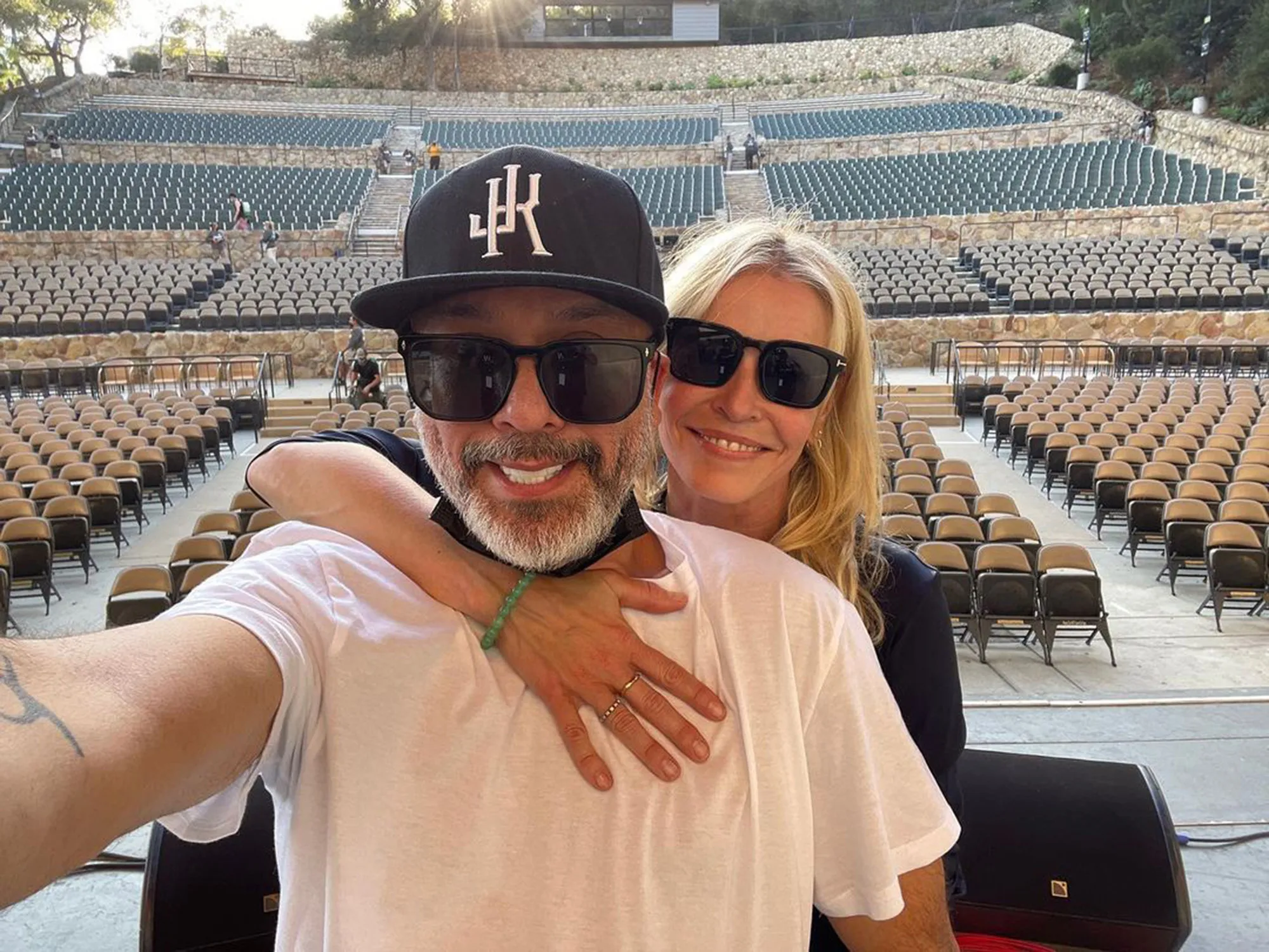 Chelsea Handler and Jo Koy pose for a selfie with an empty amphitheater behind them.