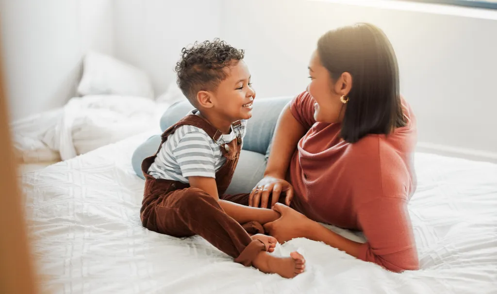 Mother and toddler son bonding and smiling on a bed.