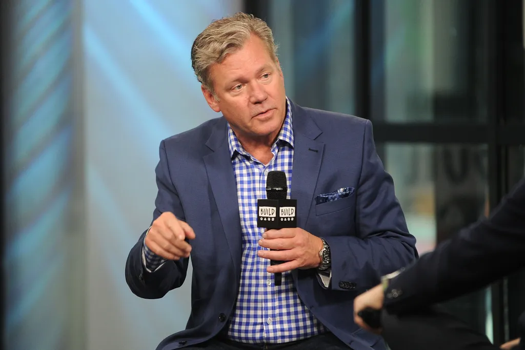 Chris Hansen, wearing a blue suit and plaid shirt, speaking into a microphone.