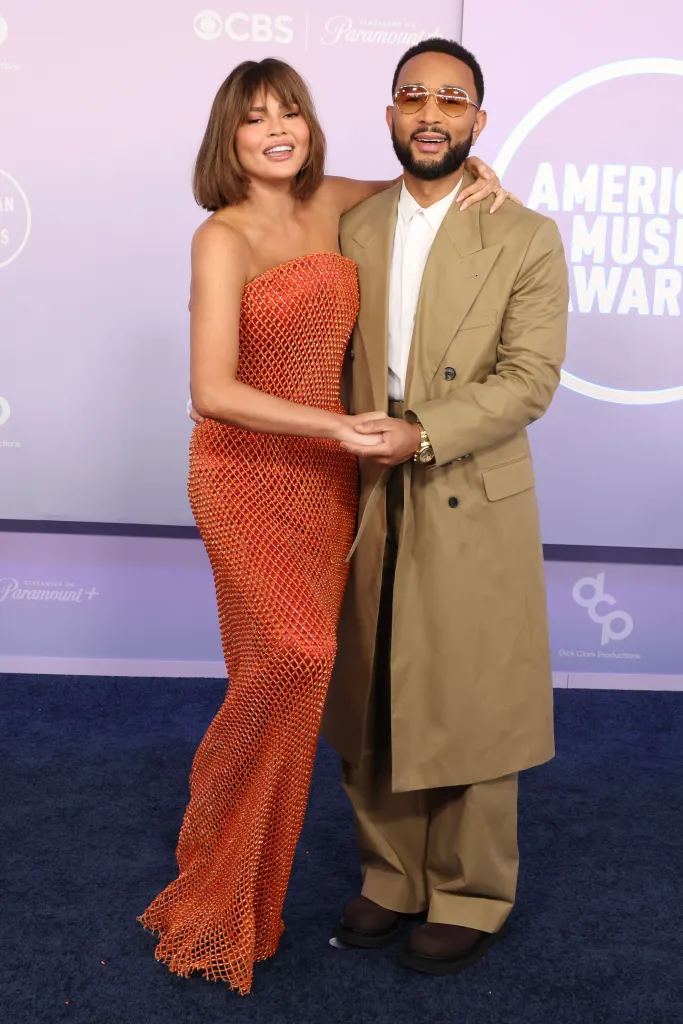 Chrissy Teigen in an orange dress and John Legend in a tan suit at the American Music Awards.