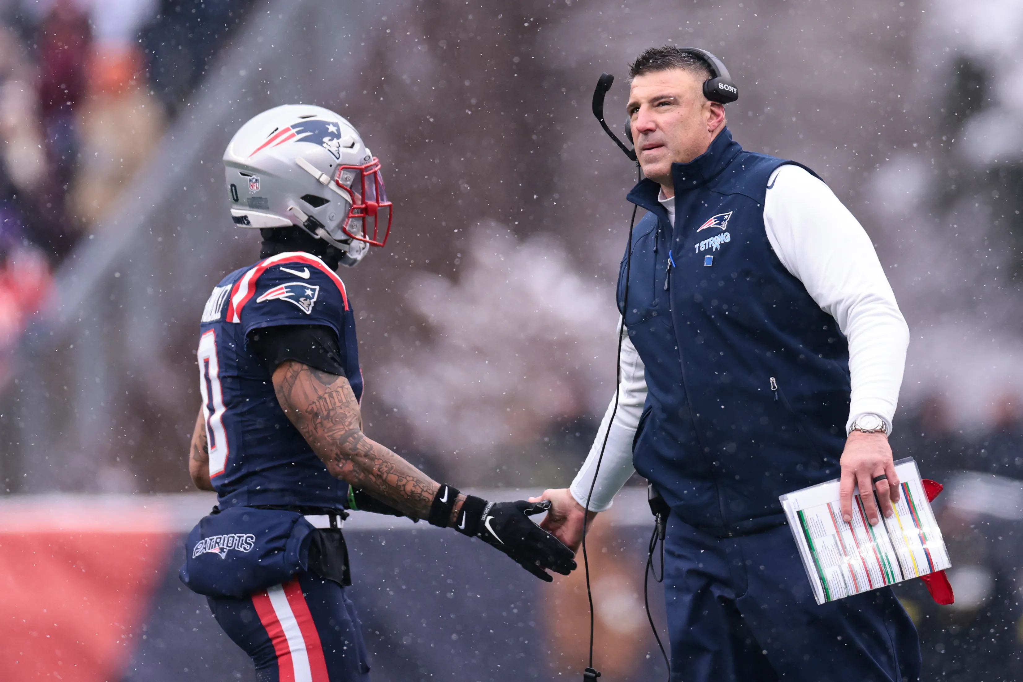 Christian Gonzalez high-fives head coach Mike Vrabel during a game.