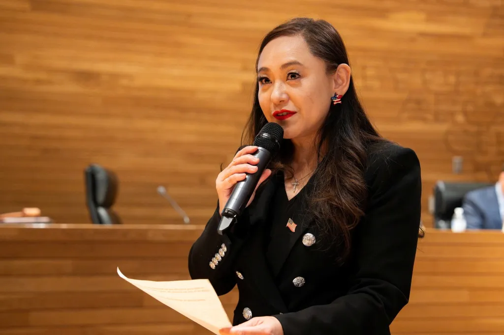 Eileen Wang speaking into a microphone while holding papers in Arcadia.