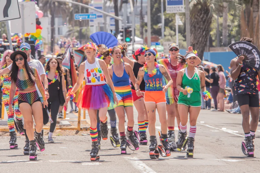 People wearing rainbow-colored clothing and jumping shoes marching in the Long Beach Pride Parade.