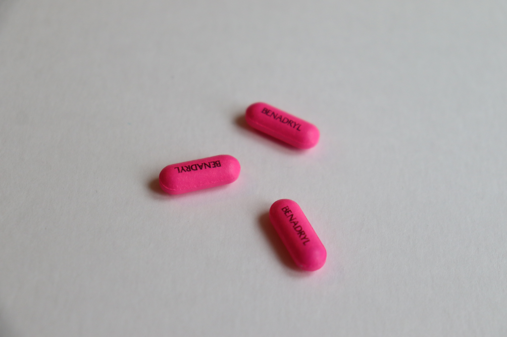 Three pink Benadryl pills are scattered on a white surface.