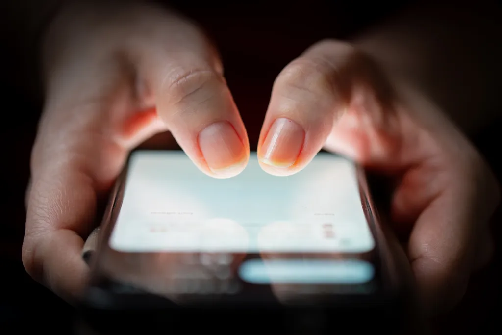 Close-up of a person's two thumbs touching a smartphone screen in the dark.