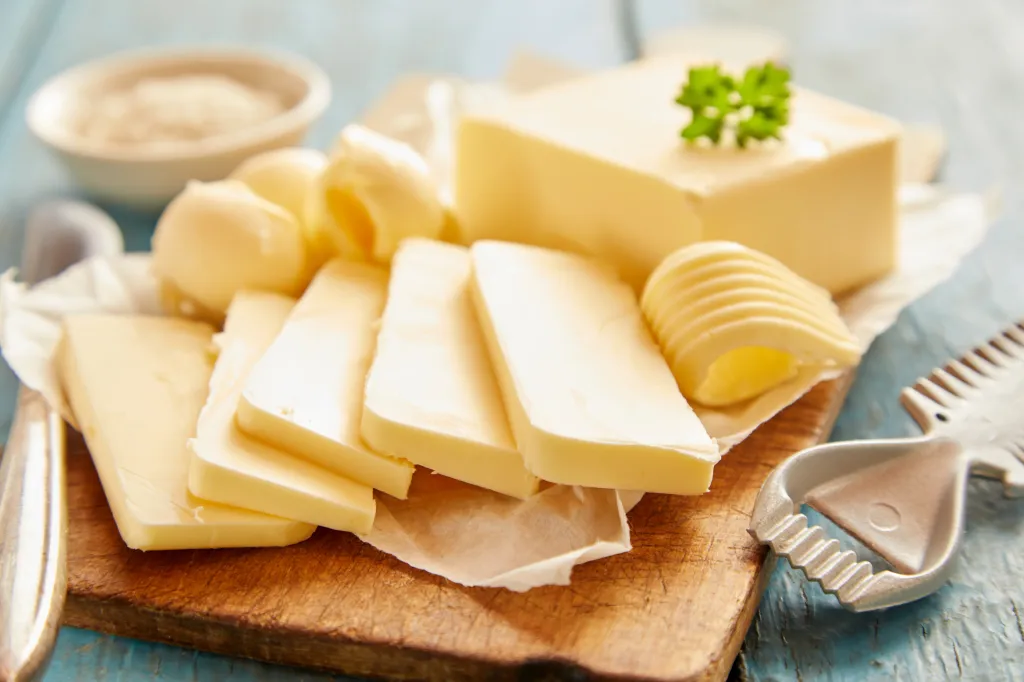 Sliced butter on a cutting board with butter curls and butter curlers.