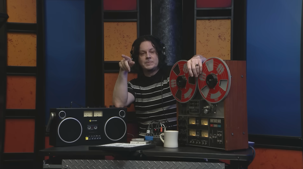 Jack White wearing headphones, pointing, with a boombox and reel-to-reel player.