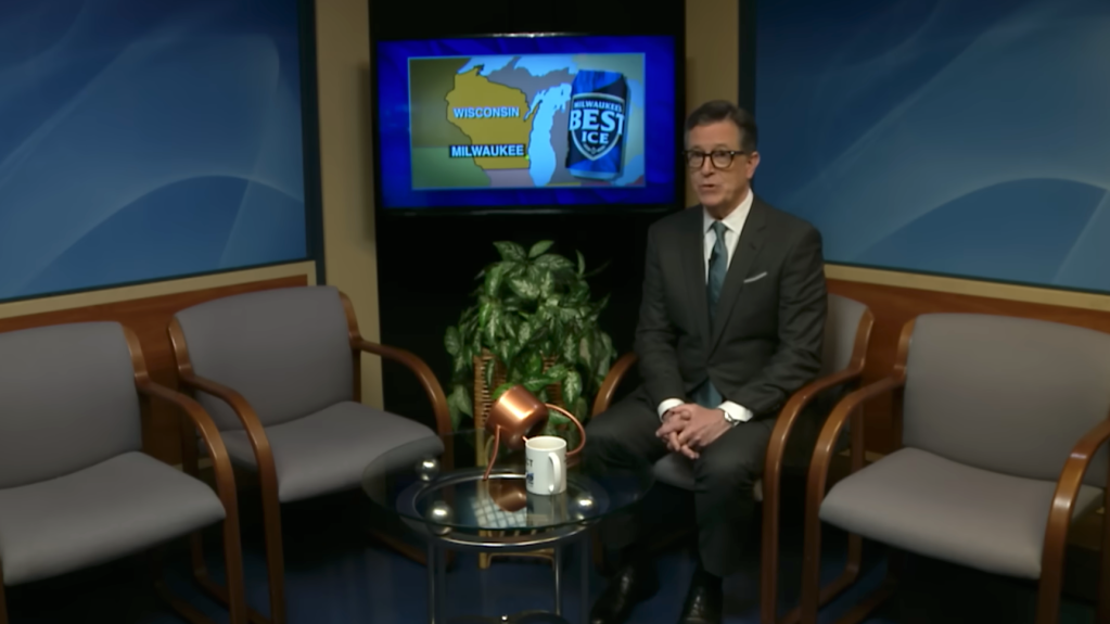 Stephen Colbert sitting on a set with a map of Wisconsin and a can of Milwaukee's Best Ice beer on a screen behind him.