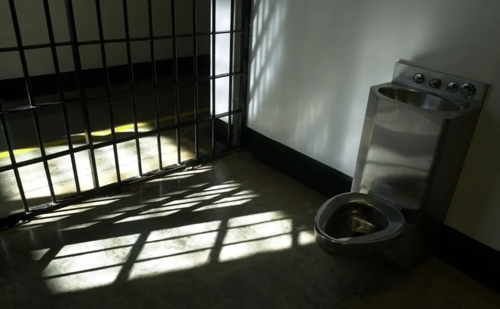 A combination sink and toilet in a prison cell with a barred door.