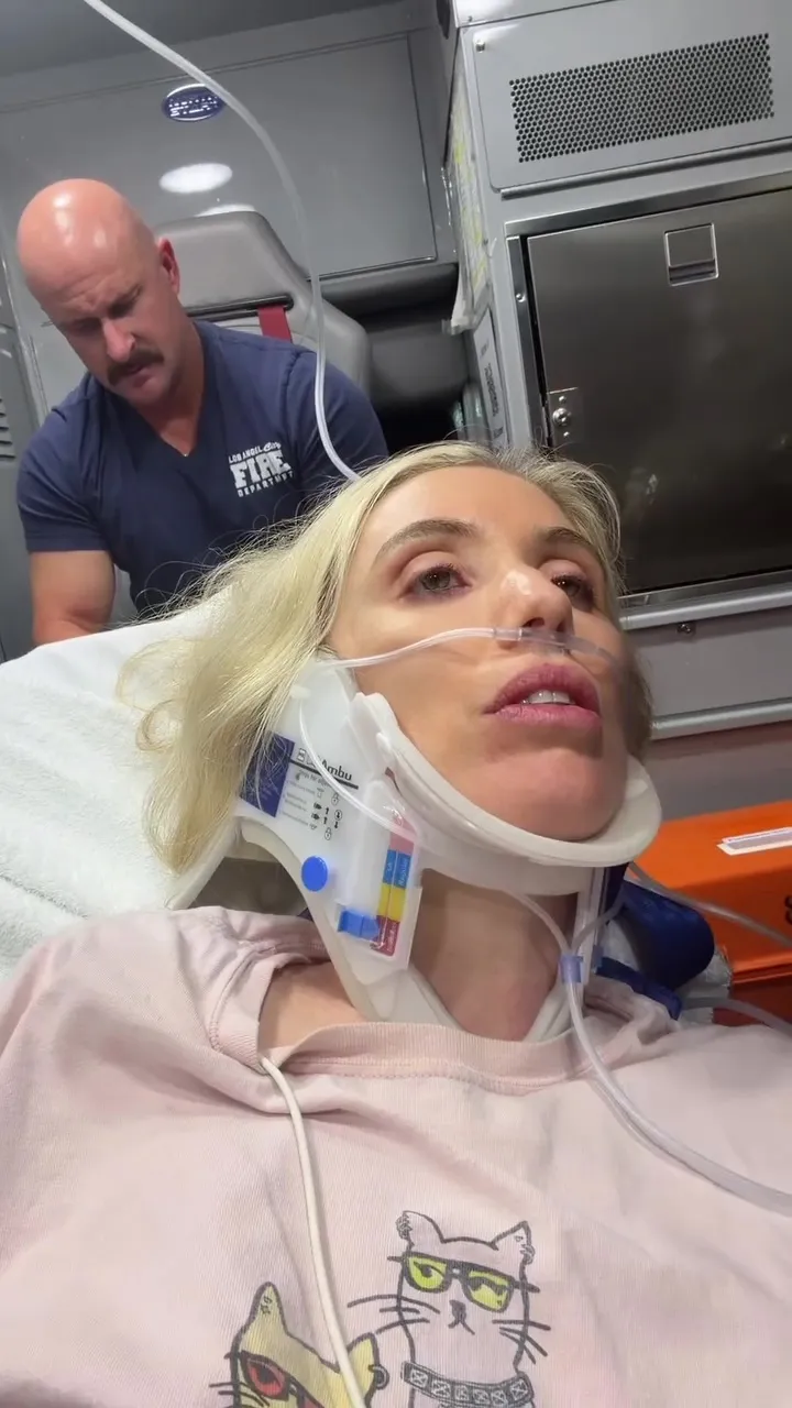 Comedian Laura Clery in a neck brace and nasal cannula in an ambulance with a first responder.