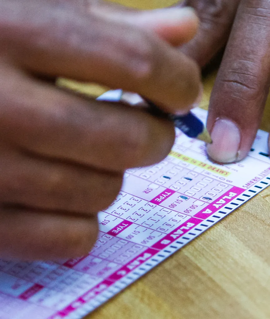 A person filling out a Powerball lottery ticket with a pen.
