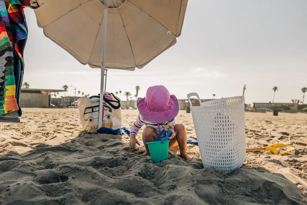 Toddler girl plays with sand toys under an umbrella at Ocean Beach.